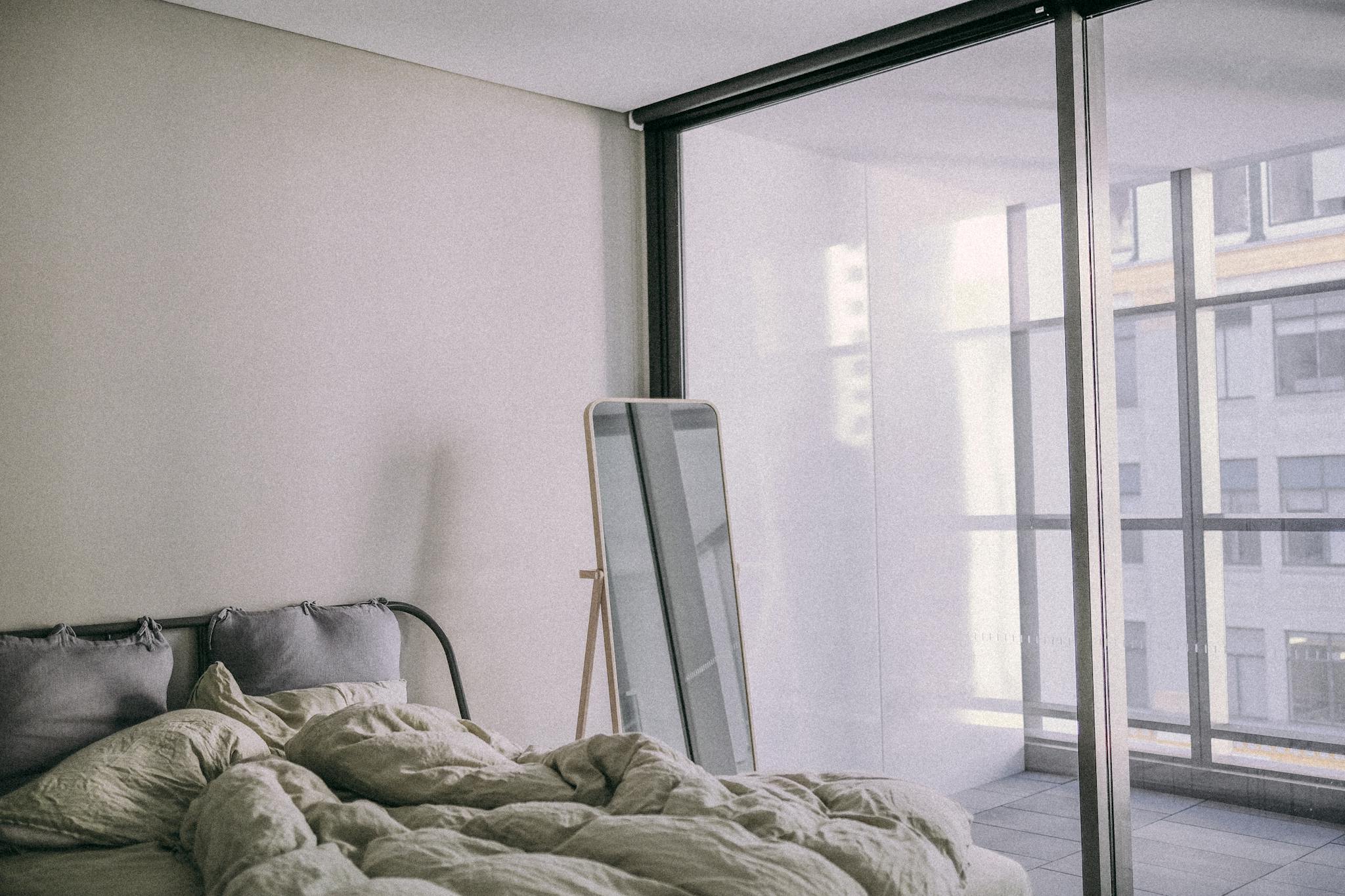 Home 3 A cozy modern bedroom with minimalistic design, featuring large glass windows and an urban view.